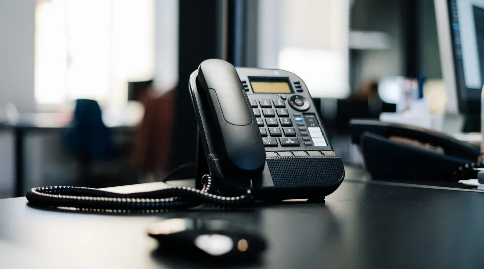 Close-up of a black desk phone with buttons on a work desk in an office setting.
